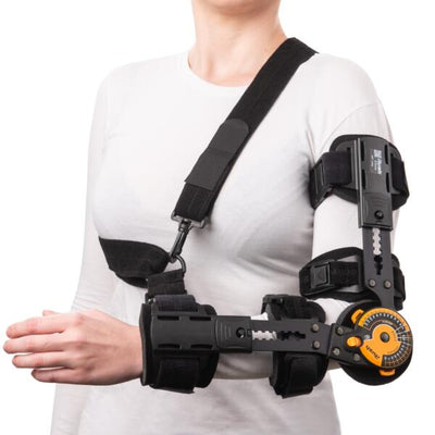 A person wearing a black shoulder and upper arm support brace with an orange dial, shown against a plain white background.